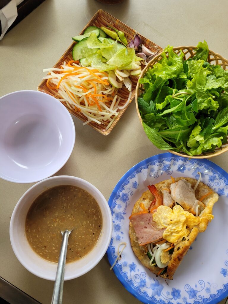 Vietnamesischer Pfannkuchen mit verschiedenen Fleischsorten, Ei, Gemüse, frischen Kräutern und Soßen.