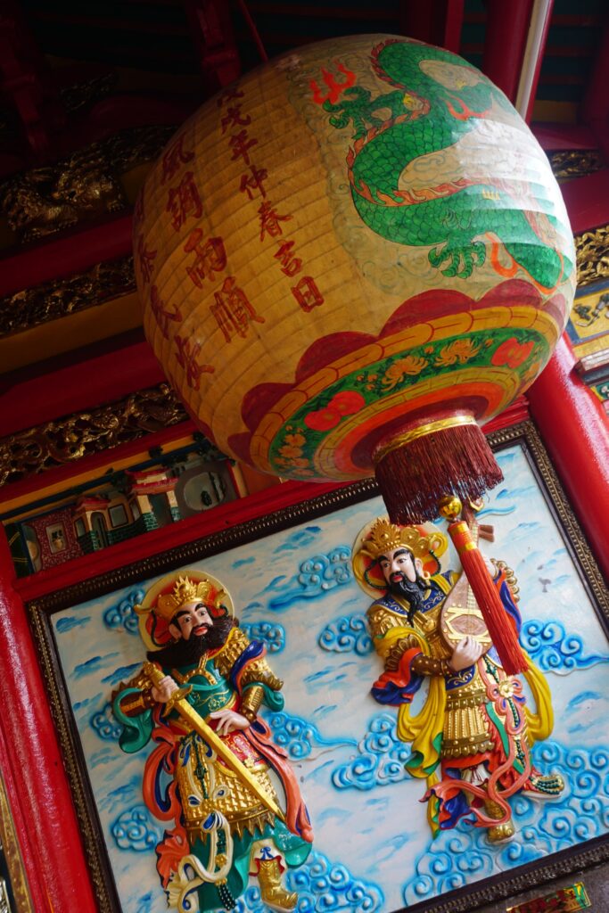 Eine chinesische Laterne mit einem bunten Relief, das zwei männliche chinesische Gottheiten abbildet, im Hintergrund.