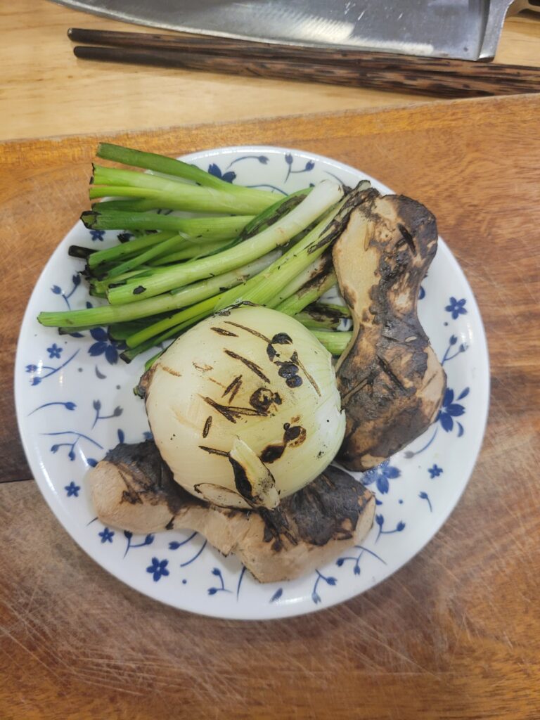 Angeröstete Zutaten für vegetarische Brühe auf einem Teller: Ingwer, Zwiebel und Lauchzwiebel.