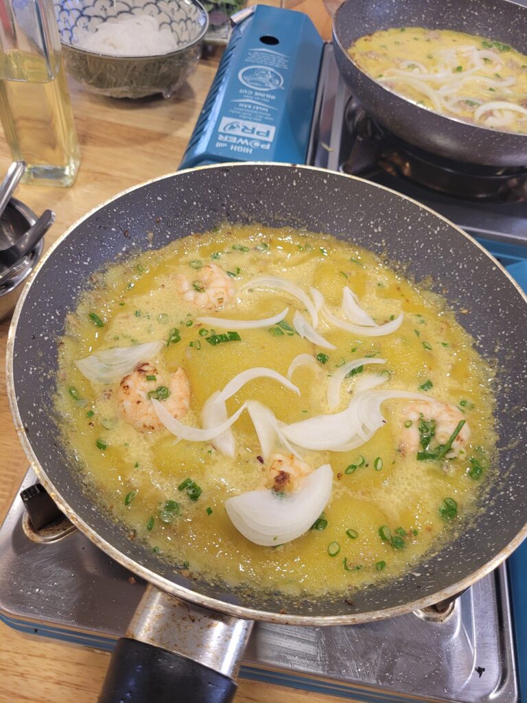Pfannkuchenteig, der mit Zwiebeln und Garnelen in einer Pfanne gebraten wird.
